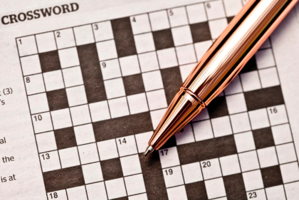 This is alt text for a photograph of a crossword puzzle and rose gold pen.