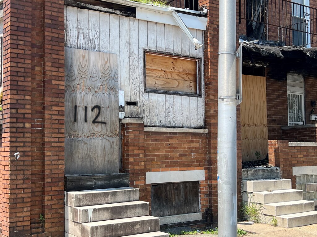 Plywood covers the doors and windows of two vacant rowhomes.